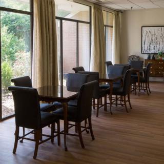 A quiet room with tables and chairs near large windows, allowing natural light to fill the space.