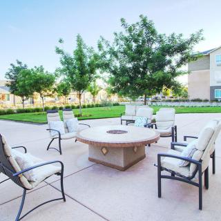 A patio with cushioned chairs arranged around a fire pit, set in a landscaped garden.