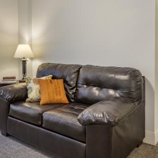 A cozy living room setup featuring a leather sofa with colorful cushions and a nearby lamp.