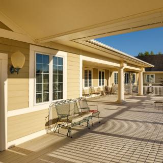 A sunny patio area with chairs, attached to a building with cream-colored siding.