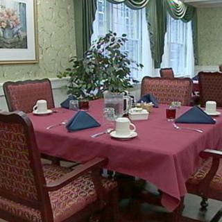 A dining table set with red tablecloth and blue napkins, surrounded by upholstered chairs.
