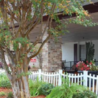 A charming house with a stone porch, surrounded by a white fence and lush garden.