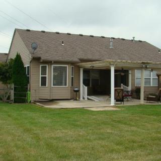 A suburban backyard featuring a house with a patio and pergola, surrounded by a well-maintained lawn.