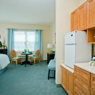 A cozy hotel room featuring a bed, kitchenette, and seating area with a table and chairs by the window.