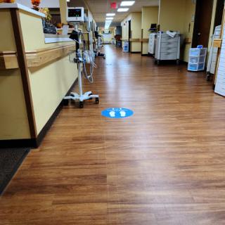 A view of a hospital hallway with wooden floors and clear directional signage on the ground.