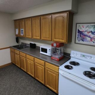 A small kitchen area with wooden cabinets, a microwave, stove, and a popcorn machine on the countertop.