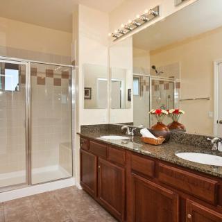 A spacious bathroom featuring a double sink vanity with granite countertops, wood cabinets, and a glass-enclosed shower.