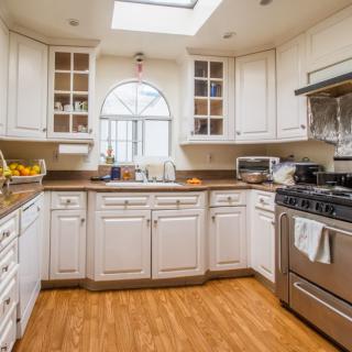 A modern kitchen with white cabinets, a stainless steel stove, and a wooden floor.