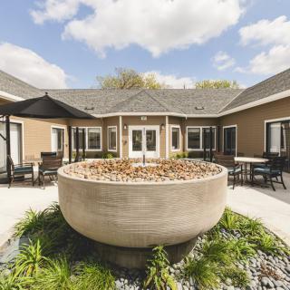A serene courtyard featuring a large stone fountain surrounded by a well-maintained landscape and a cozy building.