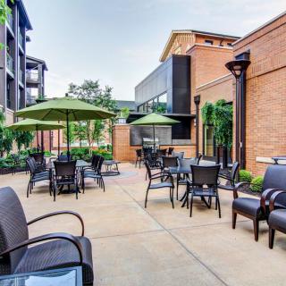 A well-furnished outdoor patio area with tables, chairs, and umbrellas set against a brick building.