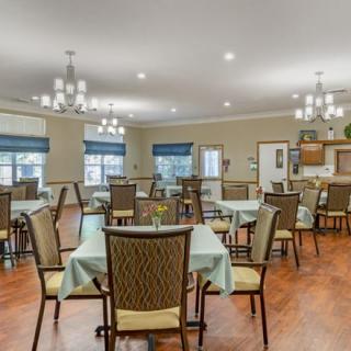 A well-lit dining area with neatly arranged tables and chairs, featuring elegant chandeliers and large windows.