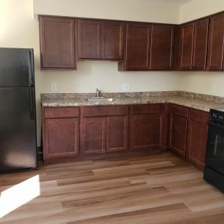 Modern kitchen with wooden cabinets and flooring, featuring a refrigerator and stove.