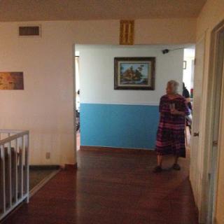 A cozy indoor hallway featuring a blue wall and an elderly woman standing thoughtfully.
