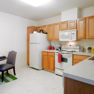 A cozy apartment kitchen with wooden cabinets, a refrigerator, and a small dining area.