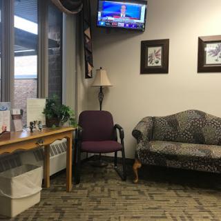 A cozy waiting room featuring a sofa, lamp, and a television with decorative elements.