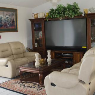 A cozy living room featuring beige leather sofas, a wooden coffee table, and a large flat-screen TV surrounded by decorative elements.