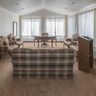 A spacious living room with a plaid sofa, multiple armchairs, and a desk near large windows with curtains.