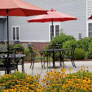 An inviting patio area with tables and red umbrellas surrounded by a vibrant garden of flowers.