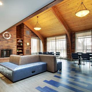 A modern living room with a high wooden ceiling, featuring a cozy sofa, fireplace, and dining area with large windows.