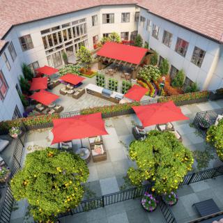 A courtyard with outdoor seating and red umbrellas, surrounded by well-maintained landscaping.