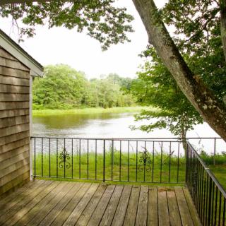 A peaceful view from a wooden deck overlooking a tranquil lake surrounded by lush greenery.