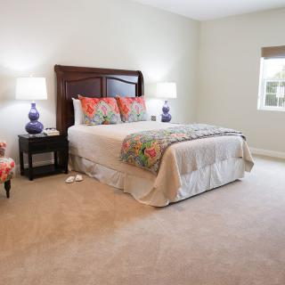 A cozy bedroom with a neatly made bed, adorned with colorful pillows and flanked by matching lamps on bedside tables.