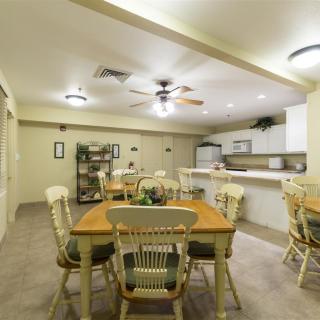 A spacious dining area connected to a kitchen, featuring wooden tables and chairs under soft lighting.
