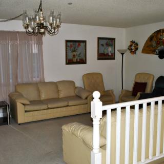 A cozy living room featuring a sofa, armchairs, and a chandelier, with artwork on the walls.