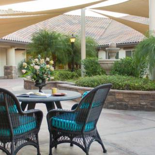 A cozy patio area with wicker chairs and a table, surrounded by lush gardens and shaded by sail canopies.