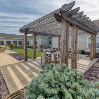 A charming patio with a wooden pergola and outdoor seating area surrounded by landscaped gardens.