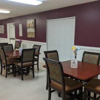 An empty dining room with neatly arranged tables and chairs against a maroon wall.