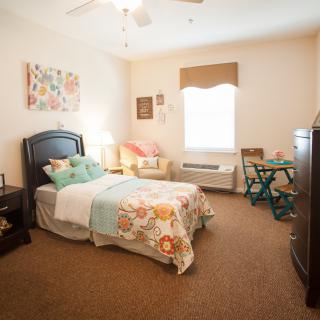 A cozy bedroom with a single bed, colorful bedding, and a small desk by the window.