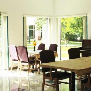 A bright dining room with large windows, featuring a wooden table and several chairs.