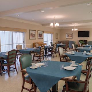 A spacious dining area featuring neatly arranged tables with blue tablecloths, complemented by comfortable chairs and warm lighting.