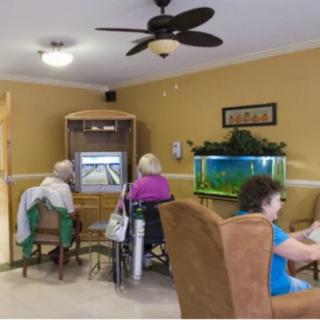 Elderly individuals sitting in a common room with a television and aquarium.