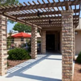 A pergola with stone columns leads to an entrance, surrounded by outdoor seating.
