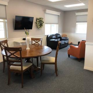 A cozy living room with a wooden dining table, chairs, a sofa, armchair, and a wall-mounted television.