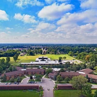 A scenic aerial view of a campus surrounded by trees and greenery under a partly cloudy sky.