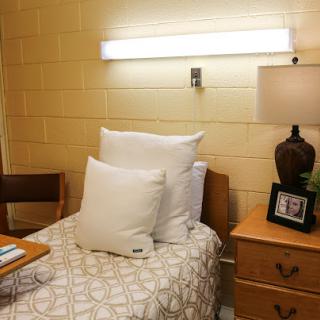 A cozy bedroom setup featuring a single bed with white pillows, a nightstand with decor, and soft lighting.