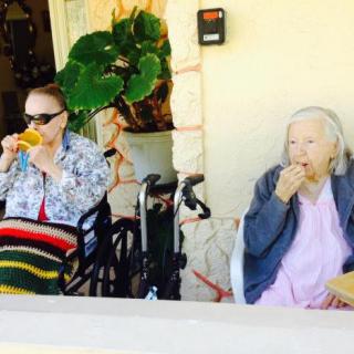Two elderly individuals enjoying a drink and a snack outdoors on a sunny day.