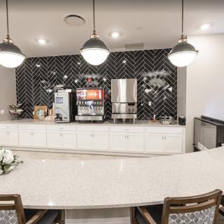 A modern kitchen space featuring a sleek countertop, pendant lights, and beverage machines.