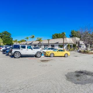 A vibrant parking lot under a clear blue sky, featuring a mix of vehicles including a yellow car and a jeep.