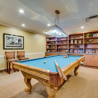 A cozy billiards room featuring a pool table, bookshelves, and warm lighting.