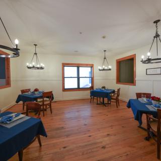 A cozy dining room with blue tablecloths, wooden floors, and elegant chandeliers.