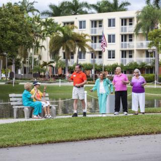 A group of seniors enjoying a day outdoors near a community building and pond.