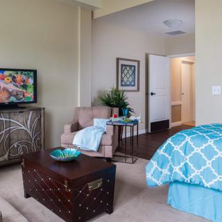 A cozy bedroom featuring a comfortable armchair, vibrant artwork, and a stylish blue bedspread.