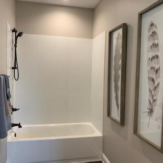 A modern bathroom featuring a bathtub with a shower, adorned with wall art and neatly hung towels.