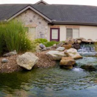 A beautifully landscaped pond with a small waterfall in front of a stone house.