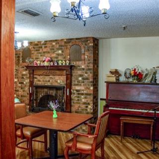 A cozy living space featuring a brick fireplace, a piano, and a dining area.