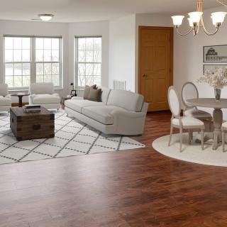 A cozy living and dining space with wood flooring, featuring a gray sofa, circular dining table, and elegant chandelier.